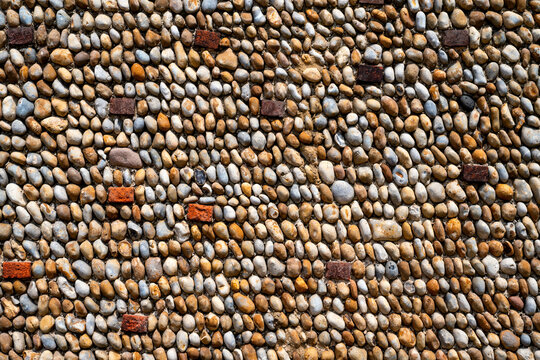 Close-up of a traditional flint and pebble stone wall facade with red brick accents, Aldeburgh, Suffolk, England. Textured surface pattern ideal for background use.