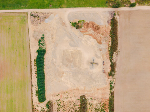 Aerial view of a gravel pit with heavy machinery and surrounding agricultural fields in Slampe parish, Tukums Municipality, Latvia.