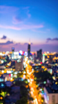Blurred city skyline with colorful bokeh lights beneath blue and pink evening sky, creating atmospheric urban night scene and vibrant traffic glow