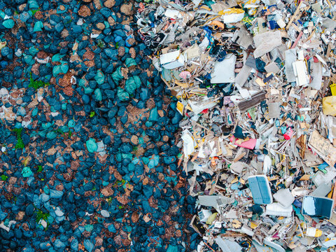 Aerial view of a waste management service facility showing a clear separation between dark blue plastic waste bags and a pile of mixed construction and household debris in Jurmala, Latvia.