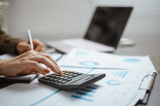 Business professional uses a calculator over charts and a laptop, demonstrating financial analysis, structured data, and detailed report. Financial calculation, accounting; financial focus.