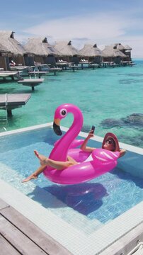 Pool Beach Vacation travel woman on inflatable Flamingo float mattress using phone in swimming pool. Girl sunbathing enjoying holidays resort pool. Raw vertical video of real woman without makeup