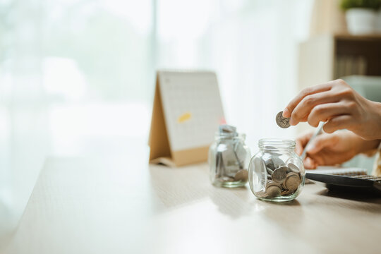 Savings concept shows a hand sorting coins among glass jars, representing financial planning, money allocation, and practical investment goals. Savings deposit, plan; savings focus.