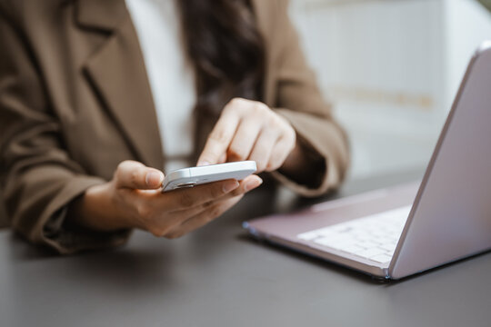 Mobile user operates a smartphone beside a laptop, representing digital finance access, connected technology, and convenient banking service. Using smartphone, social; using focus.