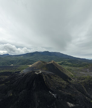 Aerial view of Paricutin volcano with dark volcanic cone, rugged lava fields, and surrounding lush green forest under a cloudy sky in San Juan Parangaricutiro, Michoacan, Mexico.