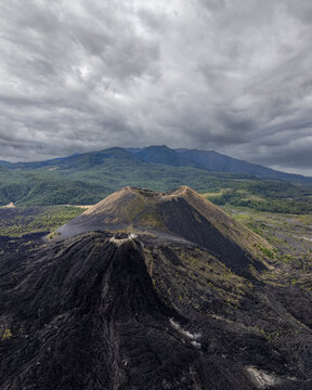 Aerial view of Paricutin volcano featuring its distinctive cinder cone, vast black lava fields, and lush mountains under a cloudy sky in San Juan Parangaricutiro, Michoacan, Mexico.