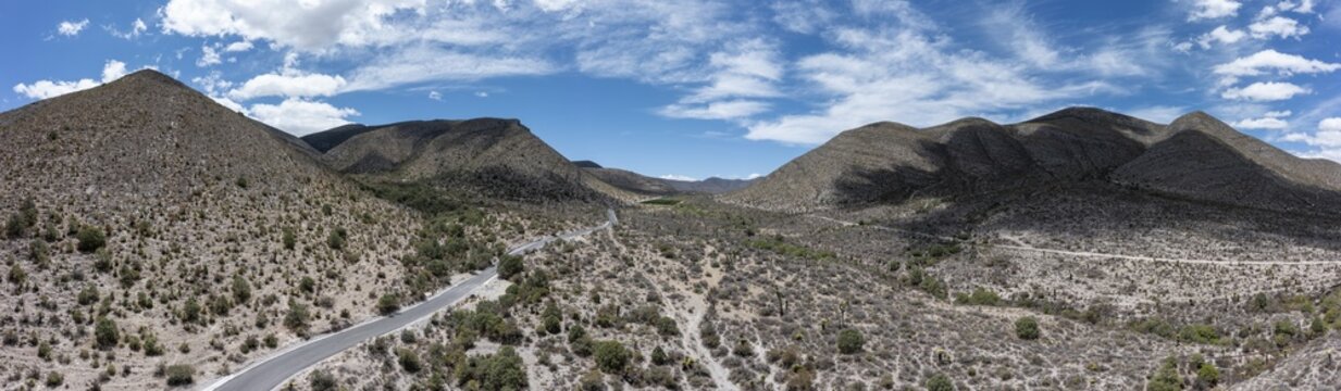Aerial view of a winding road through the arid desert landscape of the Sierra Madre Oriental mountains under a bright blue sky in Parras de la Fuente, Coahuila de Zaragoza, Mexico.