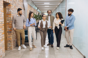 Fototapeta premium Diverse business team walking and discussing in office hallway, sharing ideas and collaborating