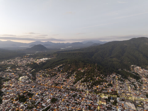 Aerial view of the city of Uruapan nestled in the lush green mountains at dusk with city lights beginning to glow in Uruapan, Michoacan, Mexico.