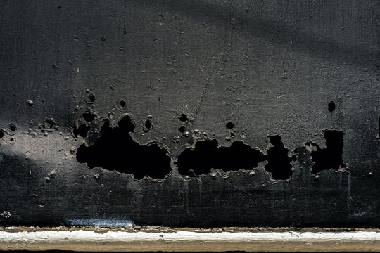 Rusty decayed black metal surface with cracked paint and corroded holes texture. Heavily weathered and corroded black metal plate.  Abstract backgrounds, Vintage themes, Representing neglect and aging