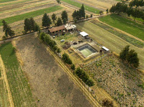 Aerial view of a rural property featuring a small building, a square pond, and surrounding agricultural fields with rows of crops and trees in Uranden de Morelos, Michoacan, Mexico.
