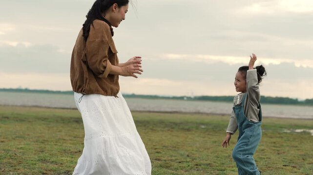 slow motion of joyful mother and daughter playing in an open field by the lake