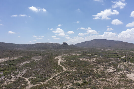 Aerial view of the arid landscape and vineyards in the desert region, featuring rugged mountains, scrub vegetation, and clear blue sky in Parras de la Fuente, Coahuila, Mexico.