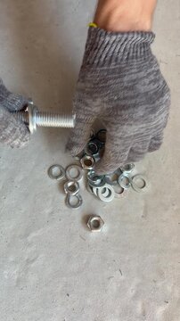 A worker assembles bolts, washers and nuts on a concrete floor. Hardware preparation