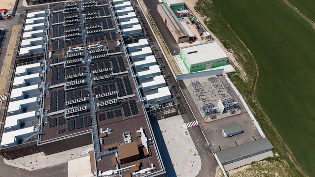 Aerial view of the Stack Infrastructure MIL04 Campus data center with rooftop solar panels, adjacent industrial facilities, and green fields in Vellezzo Bellini, Lombardy, Italy.