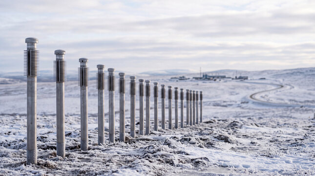 Row of steel posts in snowy winter landscape with winding road and distant buildings