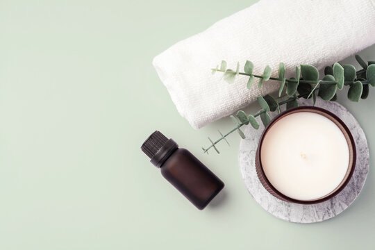 Relaxing spa concept, essential oil with aroma candle and towel on pastel green background, top view, copy space