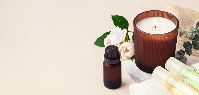 Spa and wellness background with burning aromatherapy candle, essential oil bottles and flower, copy space