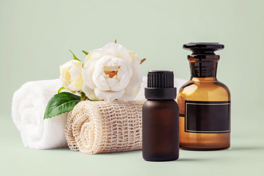 Spa and wellness composition essential oil bottles, and rolled towels with white roses on light green background