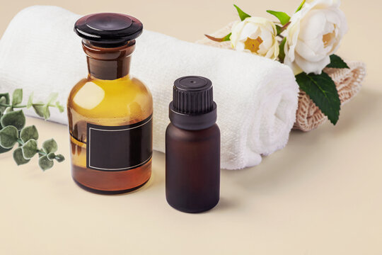 Spa concept, essential oil bottles, white towel with  roses and green leaf on beige background