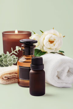Spa and wellness composition with essential oil bottles, candles, and towels with flower decoration on light green background, copy space