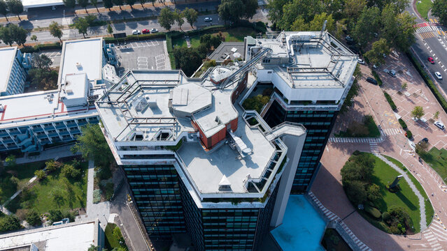 Aerial view of Eni S.p.A. 1 Palazzo Uffici headquarters with modern glass architecture, flat rooftops, and surrounding green spaces in San Donato Milanese, Lombardia, Italy.