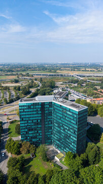 Aerial view of the Eni Palazzo Uffici office building surrounded by lush green trees and nearby highway infrastructure in San Donato Milanese, Lombardia, Italy.