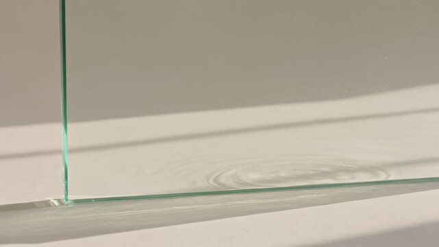 Water ripples spreading in a glass container creating concentric circles and casting shadows, clean aesthetic concept with sunlight reflecting on the calm water surface