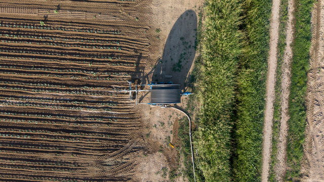 Aerial view of a hose reel irrigator watering an agricultural field with rows of crops and lush vegetation in Mediglia, Lombardy, Italy.