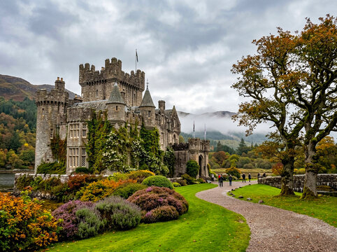 Medieval stone castle featuring classic battlements and ivy covered walls standing within a lush green landscape during a cloudy day