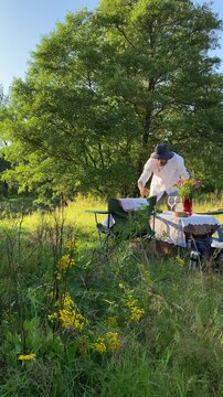 A man enjoys a meal at a picnic table in tall grass, and savoring everyday moments in the fresh summer air. An atmospheric spot for outdoor relaxation