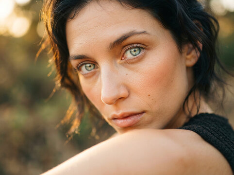 Beautiful young woman with piercing green eyes looking directly into the camera during a warm golden hour outdoor sunset portrait