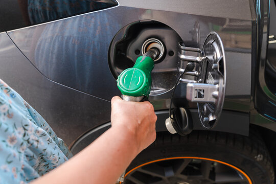 Hand refueling gray car with green fuel nozzle