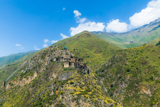 Aerial view of the historic medieval village of Mutso perched on a rocky mountain ridge, surrounded by lush green slopes and a clear blue sky in Mutso, Mtskheta-Mtianeti, Georgia.