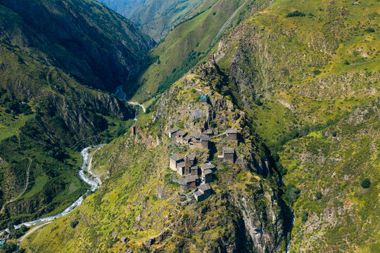 Aerial view of the historic medieval village of Mutso perched on a rocky mountain ridge surrounded by lush green slopes and a river valley in Mutso, Mtskheta-Mtianeti, Georgia.