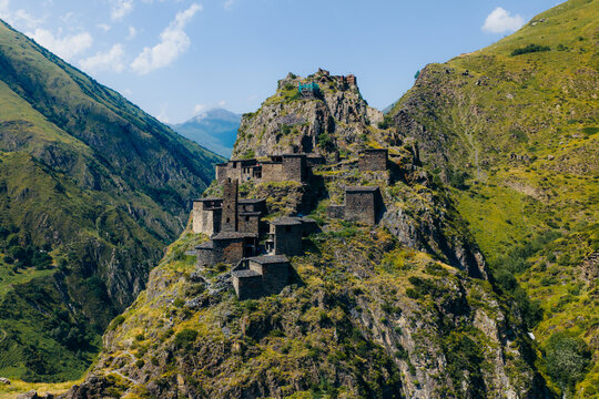 Aerial view of the medieval village of Mutso perched on a rocky ridge, featuring ancient stone towers and dwellings surrounded by green slopes in Mutso, Mtskheta-Mtianeti, Georgia.