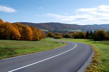 Obraz premium Scenic Country Road Weaving Through Autumn Trees and Rolling Hills Under a Blue Sky