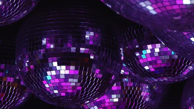A mesmerizing display of numerous disco balls hangs, catching and scattering brilliant beams of green, orange, red, and blue light across a dark festive space.