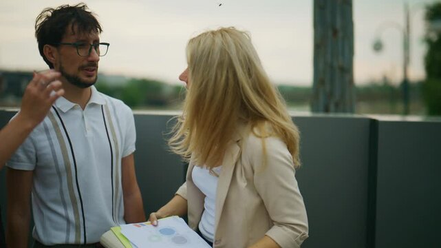 Three colleagues are engaged in a serious discussion, reviewing business documents outdoors. A professional team collaborates on project plans, analyzing data in an urban setting.