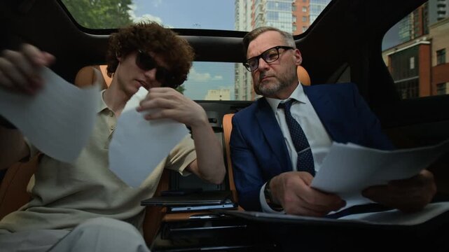 Middle aged Caucasian businessman and young adult partner reviewing documents in car, young man tearing up contract. Clip represents business conflict, contract rejection and failed partnership