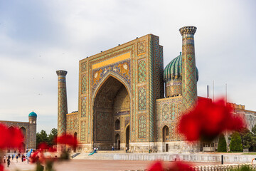 Obraz premium Sher-Dor Madrasah Framed by Red Flowers at Registan Square in Samarkand