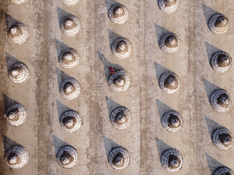 Aerial view of traditional wooden conical paddy storage structures arranged in rows on the ground with a person walking among them in Brahmanbaria, Chittagong Division, Bangladesh.