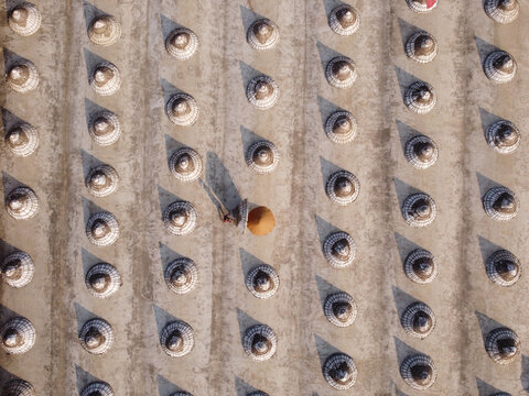 Aerial view of rows of cone-shaped paddy storage structures with a person walking through the field casting long shadows in Brahmanbaria, Chittagong Division, Bangladesh.