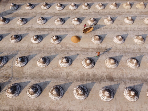 Aerial view of traditional conical paddy storage structures arranged in rows on a drying ground with workers tending to the harvest in Brahmanbaria, Chittagong Division, Bangladesh.