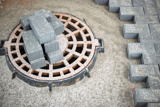Construction of a sidewalk featuring brick pavers around a manhole cover in an urban setting