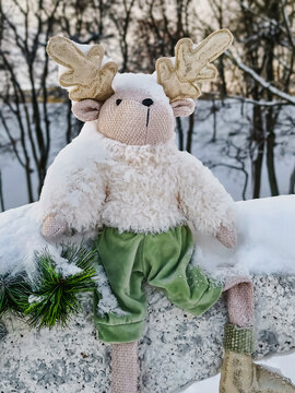 A decorated natural Christmas tree stands outdoors in a snowy area. There is a soft toy reindeer sitting near the tree, adding to the winter spirit