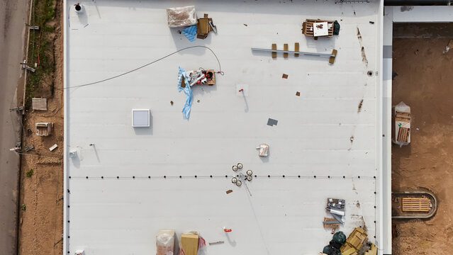 Aerial view of a flat white roof under construction with scattered building materials, pallets, and equipment in Riga, Latvia.