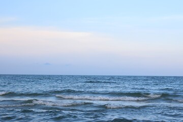 Fototapeta premium Calm Ocean Waves Rolling onto Sandy Shore with Blue Sky and Soft Clouds