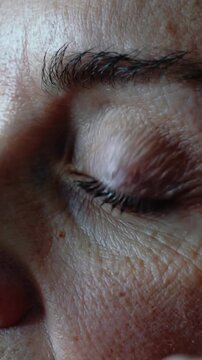Vertical video: Pressing index finger, woman rubbing upper eyelid on pillow, lamp glowing