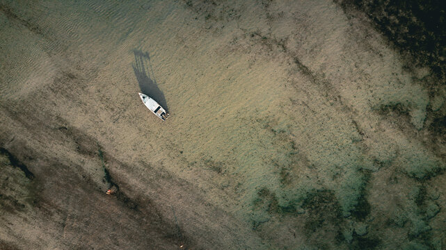 Aerial view of a small boat anchored in the clear, shallow turquoise waters off Gili Trawangan, with sandy seabed patterns visible Pemenang, West Nusa Tenggara, Indonesia.